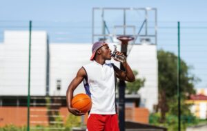 Young black basketball player drinking water to refresh himself after training on outdoor court