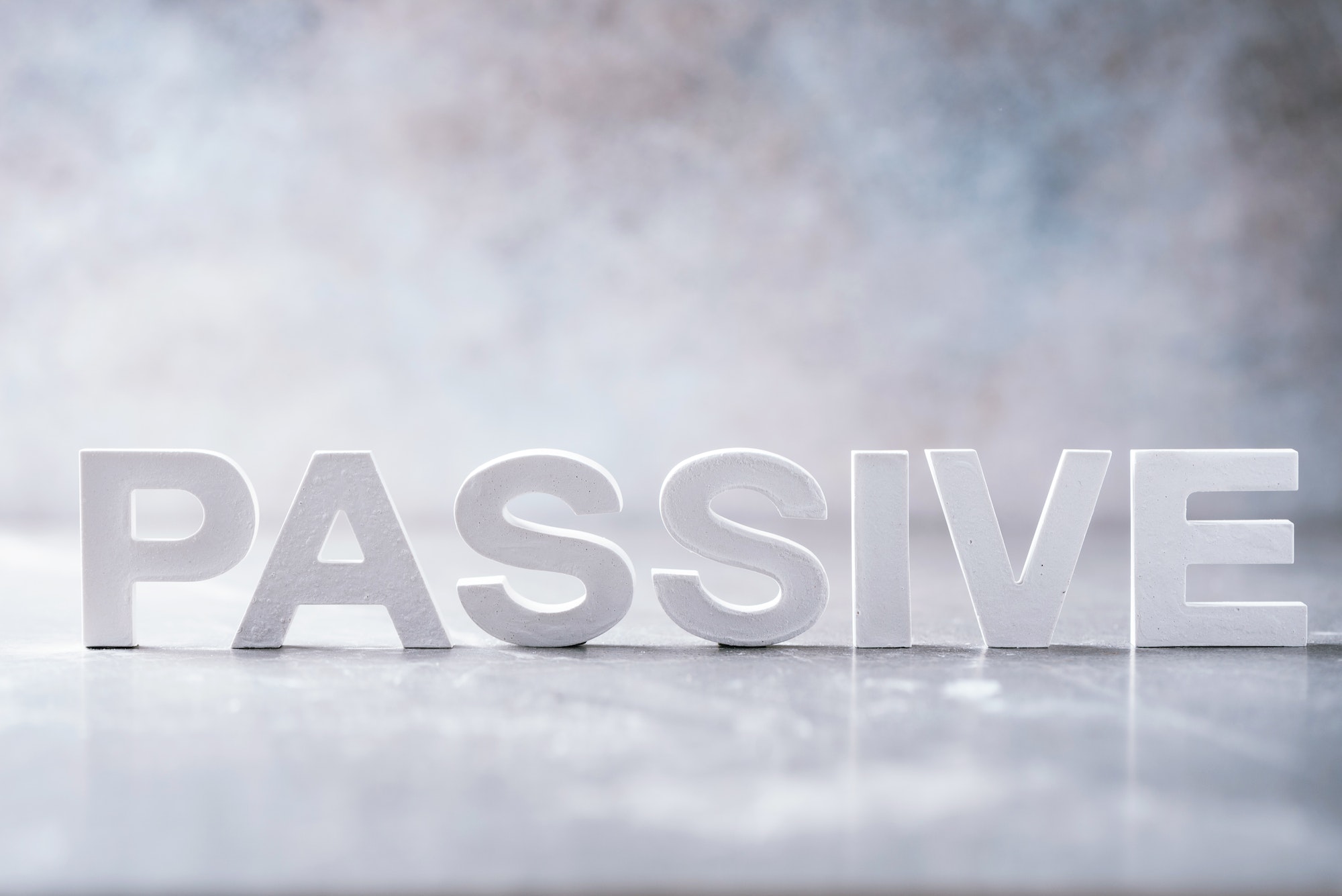Word PASSIVE made with cement letters on grey marble background. Copy space. Business concept